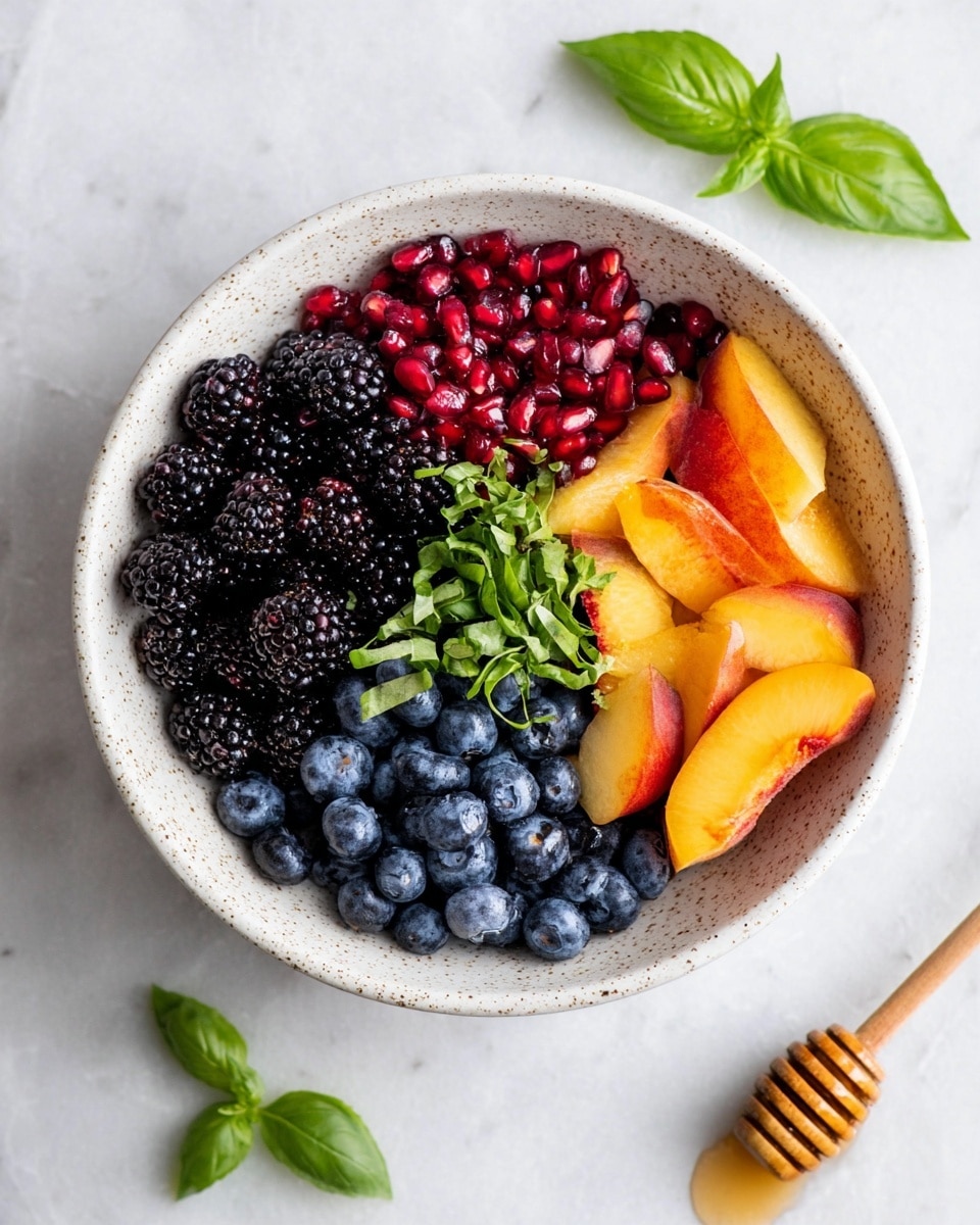 A white bowl filled with a bright fruit salad showing several layers of colorful fruits. At the bottom and mixed throughout are dark blackberries with a bumpy texture. There are also round, deep blue blueberries scattered around. On top of these, juicy orange-yellow slices of peach or nectarine with smooth skin and a glossy finish are placed. Bright red pomegranate seeds, small and shiny, add a pop of color spread evenly over the fruit. Thin strips of fresh green basil are sprinkled across the salad, adding a bright green contrast. The bowl sits on a white marbled surface, and a silver spoon is tucked into the side of the bowl. photo taken with an iphone --ar 4:5 --v 7