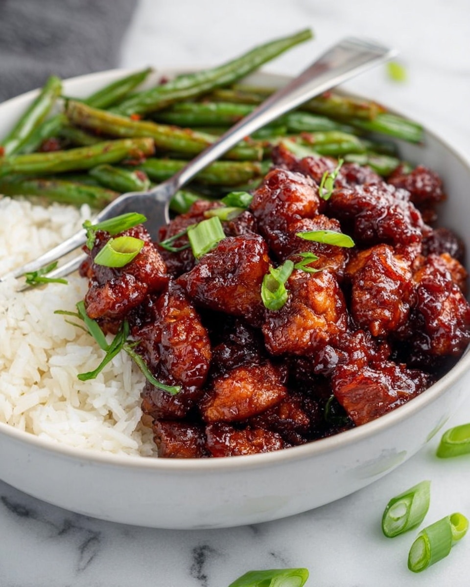 A close-up image shows a silver fork holding a shiny, sticky, dark red piece of glazed chicken with small green onion slices on top. Below the fork, pieces of the same glazed chicken fill a shallow white bowl. Behind the chicken in the bowl, there are several cooked green beans arranged loosely. The whole scene is set on a clean white marbled surface with some scattered green onion slices around. The colors focus on the glossy dark red glaze, vibrant green of the onions and green beans, and the white of the bowl. photo taken with an iphone --ar 4:5 --v 7