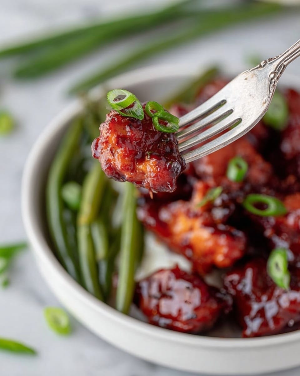 A white bowl holds a serving of sticky, dark reddish-brown glazed chicken pieces garnished with small green onion slices on top. Behind the chicken, there is a layer of cooked green beans with a slightly browned texture, and to the left, a portion of white rice completes the dish. A silver fork rests inside the bowl near the green beans. The bowl is set on a white marbled surface, with a few green onion slices scattered nearby. Photo taken with an iphone --ar 4:5 --v 7