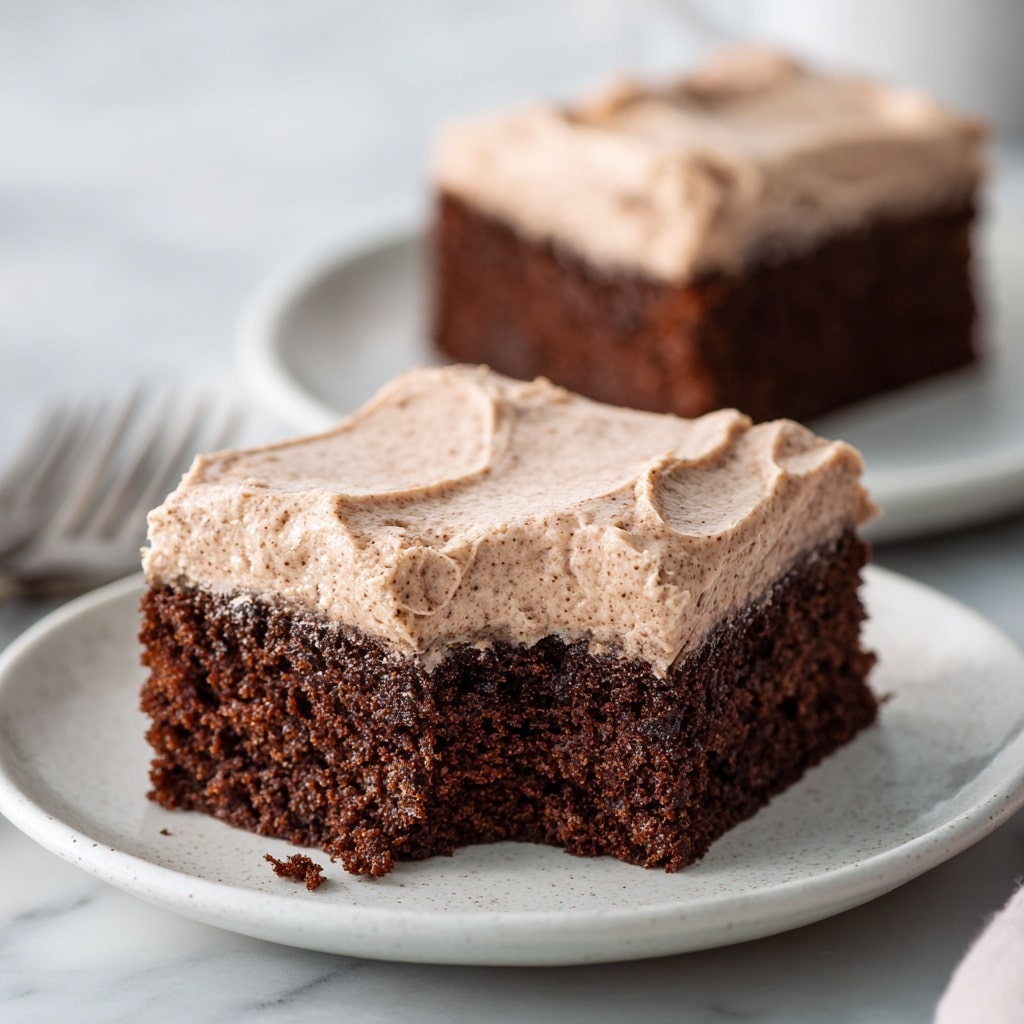 A close-up image of a single square piece of rich, dark brown chocolate brownie with a smooth, shiny light caramel-colored frosting layer on top, about one layer thick, showing a slightly swirled texture. The brownie looks moist and dense with a crumbly texture at the sides. The background is a white marbled texture beneath the brownie with some scattered crumbs, and a blurred larger piece of the same brownie is visible behind it. Photo taken with an iphone --ar 4:5 --v 7