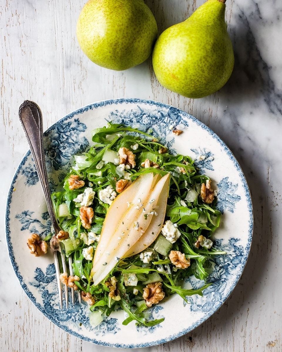 A white plate with a blue floral pattern holds a layered pear salad consisting of five thin, light green and white pear slices stacked in the middle. The pears are surrounded by fresh, bright green arugula leaves scattered around the plate. Walnut pieces and small chunks of creamy, white-blue cheese are sprinkled over the arugula. A silver spoon drizzles a thick, beige dressing over the top pear slice. The plate sits on a white marbled surface with a blurred green pear in the background. photo taken with an iphone --ar 4:5 --v 7