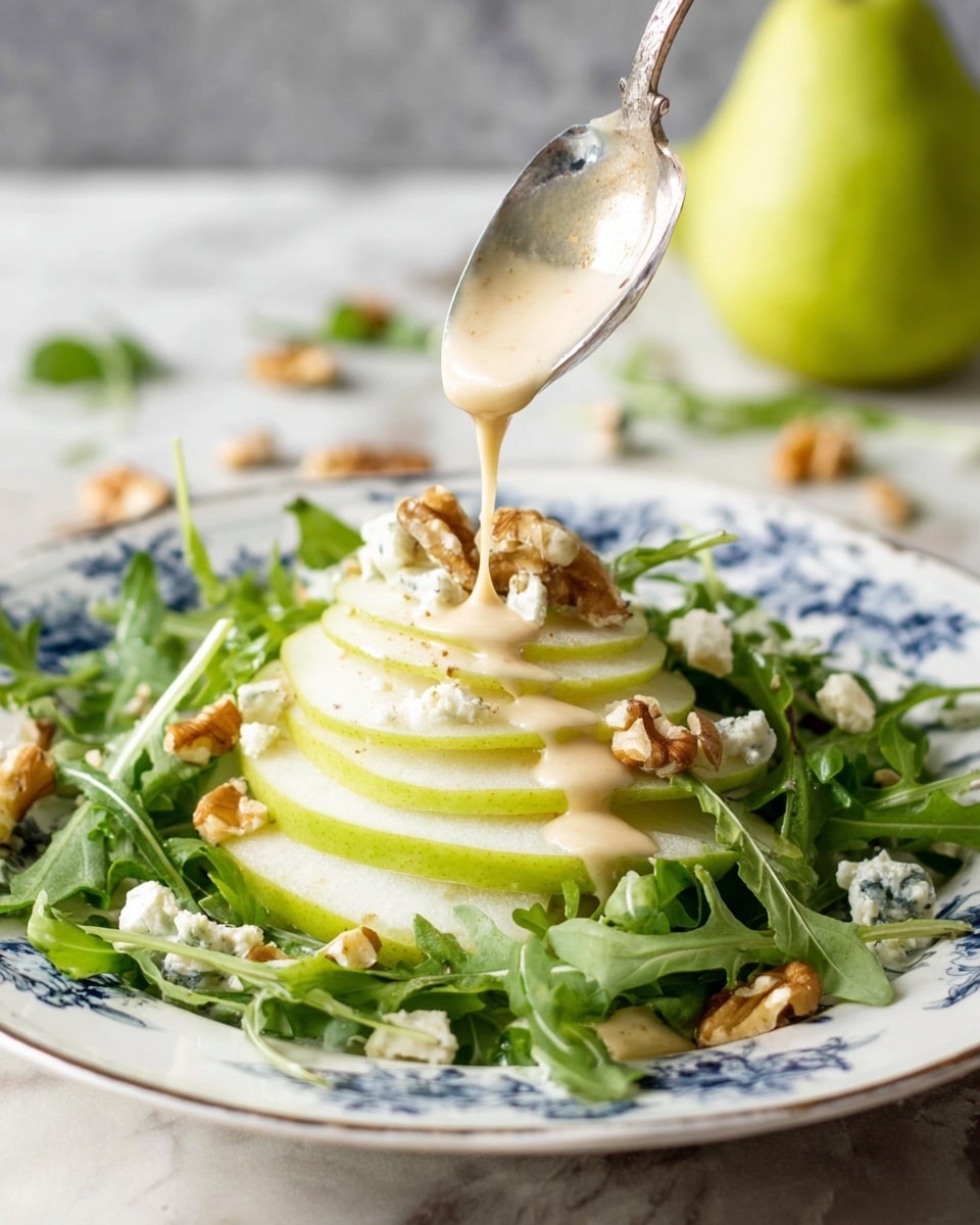A white plate with blue floral patterns holds a fresh salad with three main layers: the bottom green layer consists of loose arugula leaves with a slightly rough texture, the middle layer features two thin, translucent pear slices positioned in the center with pear skin on the edges, and the top layer is made up of scattered small chunks of creamy blue cheese and light brown walnut pieces. A silver fork rests on the left edge of the plate, partially on the salad. The plate is placed on a white marbled surface, with two whole green pears positioned above it. Photo taken with an iphone --ar 4:5 --v 7
