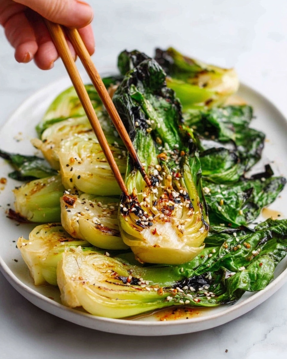 The image shows a white plate filled with grilled baby bok choy arranged in layers. Each piece has a bright green leafy top and a white to light brown grilled bottom with visible char marks. The texture of the grilled side looks slightly crispy with some sesame seeds sprinkled over it. A woman's hand is using wooden chopsticks to pick up one piece. The background is a white marbled surface. photo taken with an iphone --ar 4:5 --v 7