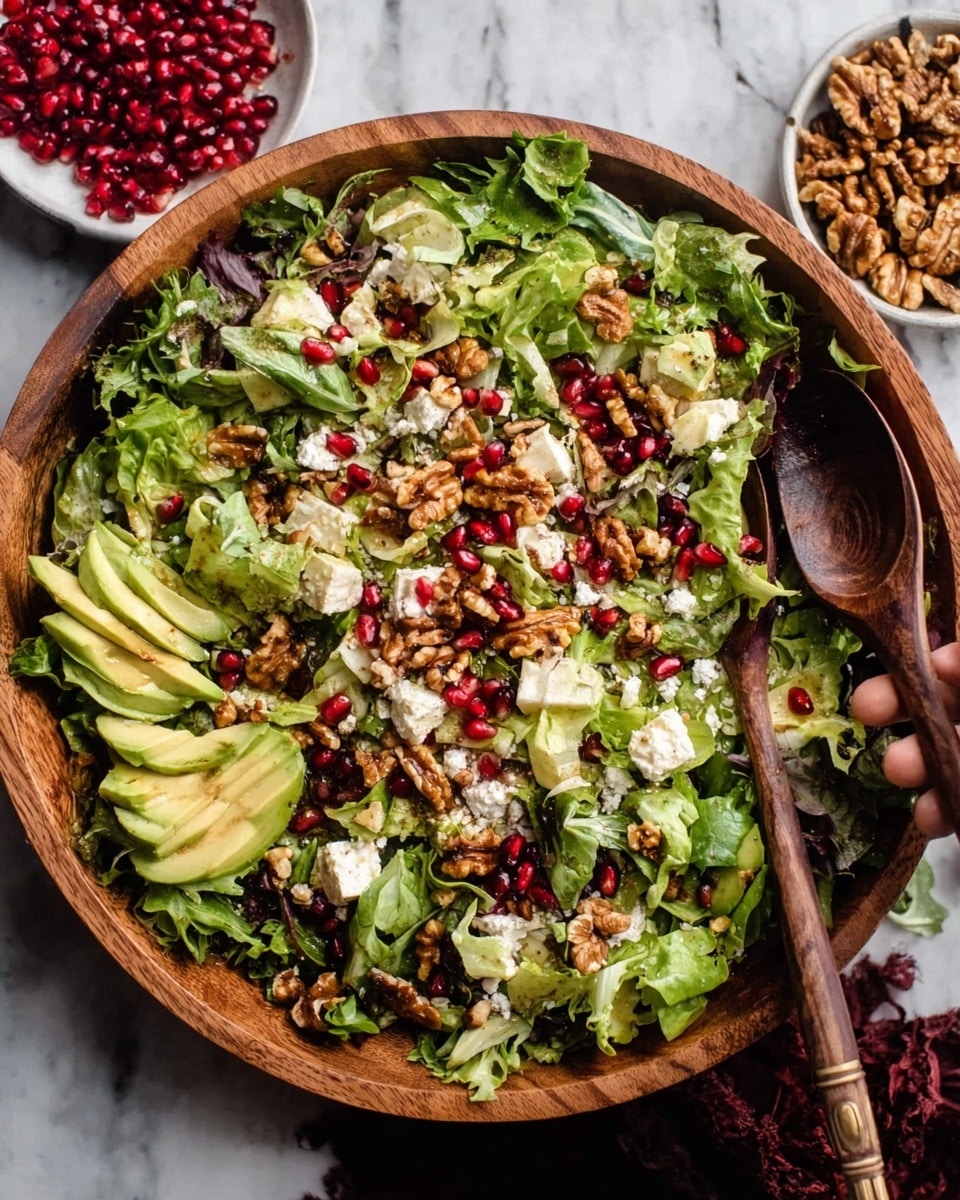 A large round wooden bowl filled with a fresh mixed green salad placed on a white marbled surface. The salad has several layers: a base of leafy greens with different shades of green, topped with chunks of light creamy cheese, bright red pomegranate seeds scattered evenly, small pieces of brown toasted walnuts, and thin slices of creamy avocado arranged on one side. A woman's hand is holding a dark brown wooden spoon poised over the salad, ready to serve. Nearby, a small white bowl filled with walnuts and another with pomegranate seeds sit on the side. The photo taken with an iphone --ar 4:5 --v 7