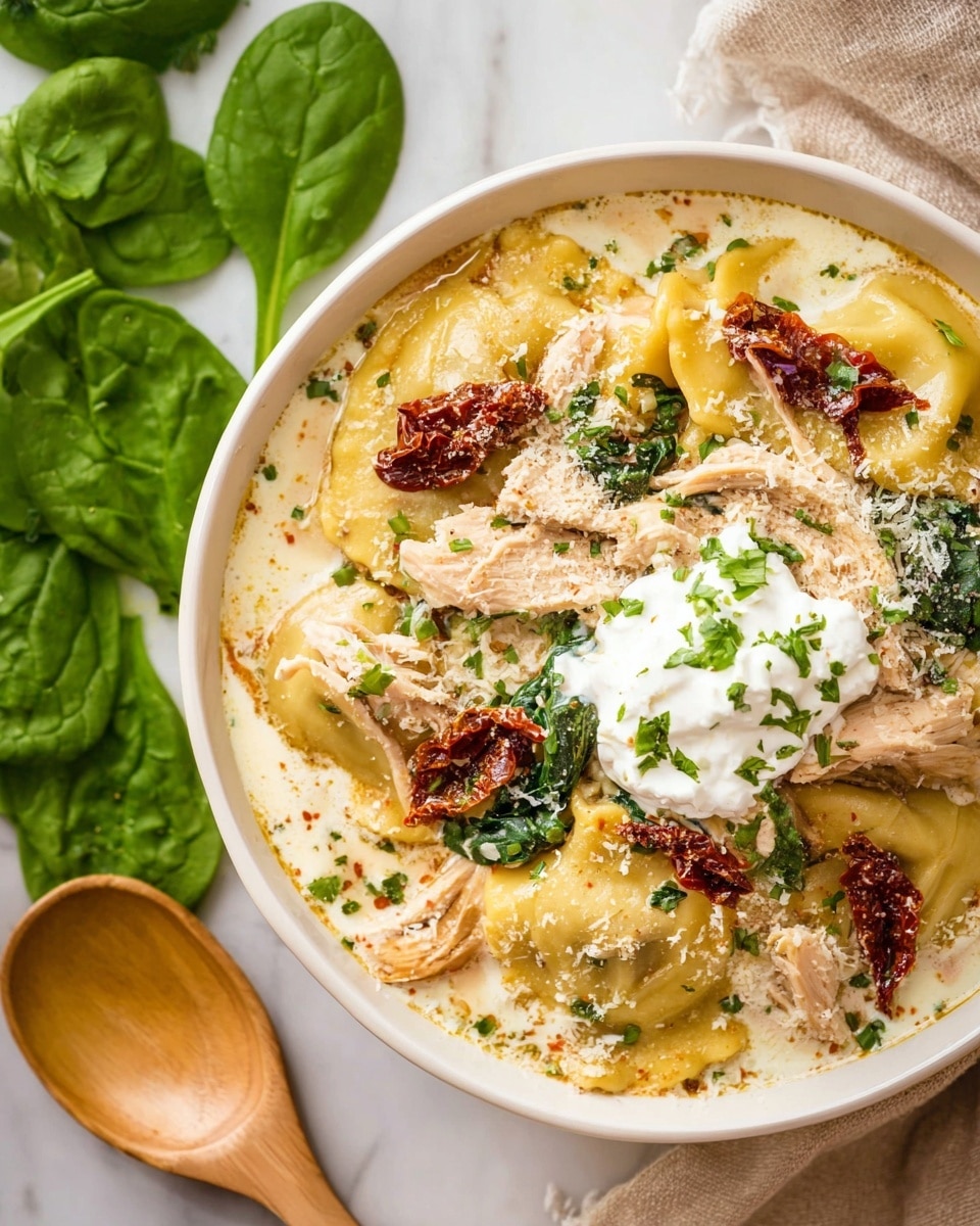 A white bowl filled with creamy pasta showing three main layers: the bottom layer is smooth, light beige creamy sauce, above it are yellow ravioli mixed with pieces of shredded brown chicken and dark green spinach leaves, scattered with dried red sun-dried tomatoes; the top layer has a dollop of white cheese cream garnished with finely chopped green herbs, all sprinkled lightly with grated cheese. The bowl sits on a white marbled surface with some fresh spinach leaves and wooden spoons nearby. photo taken with an iphone --ar 4:5 --v 7
