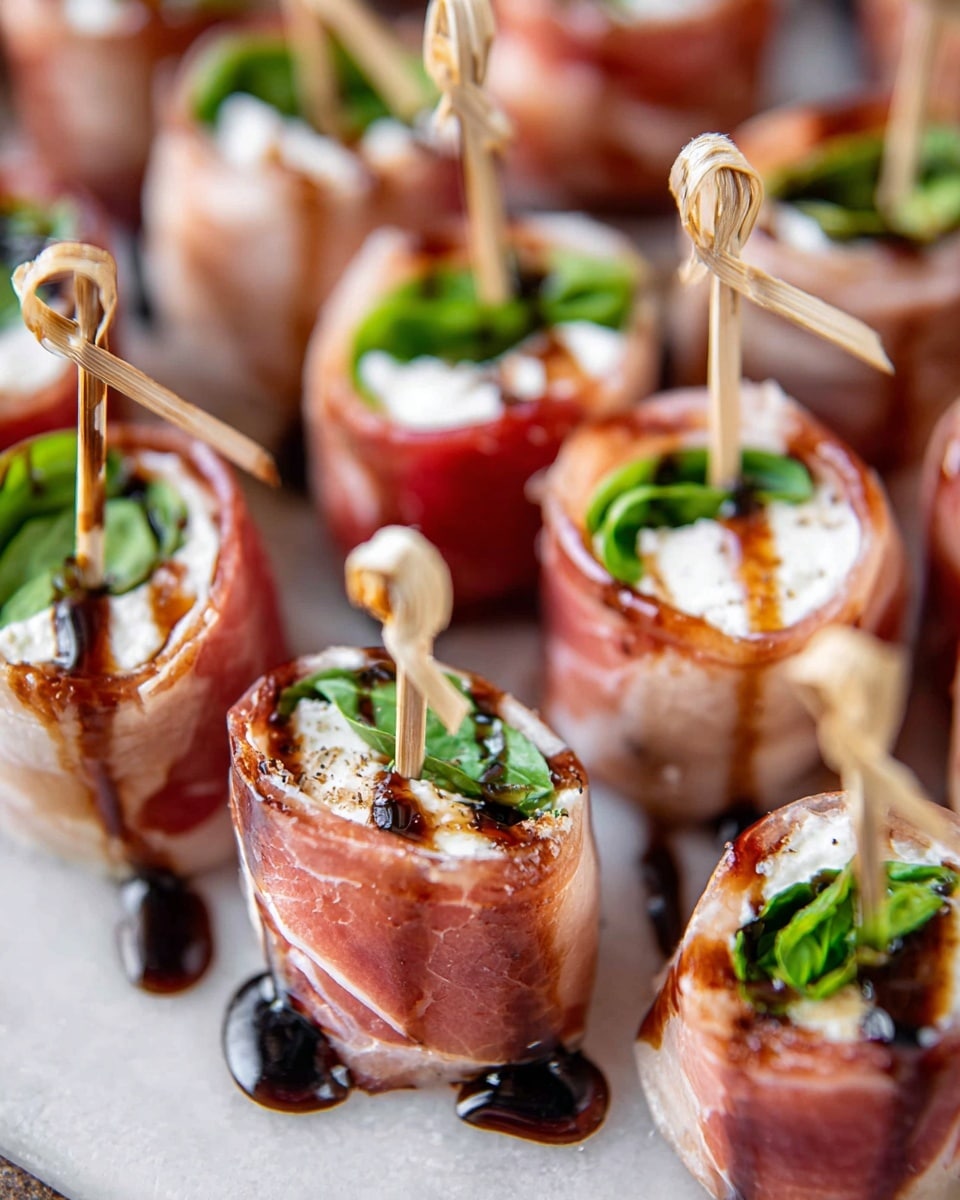A round beige ceramic plate holds about twenty small appetizers, each made of three layers: a white soft cheese ball, wrapped in thin pink prosciutto with some green basil leaves peeking out, all secured with a light brown bamboo pick that has a knot at the top; the prosciutto has a shiny texture and is drizzled with a dark brown balsamic glaze. Around the plate are toasted round bread slices, small yellow and red tomatoes, fresh basil leaves, and a striped blue and white cloth with extra bamboo picks, all set on a wooden surface with a white marbled texture showing at the edges. A white bowl filled with more white cheese balls sprinkled with herbs is partially visible in the top left corner. Photo taken with an iphone --ar 4:5 --v 7