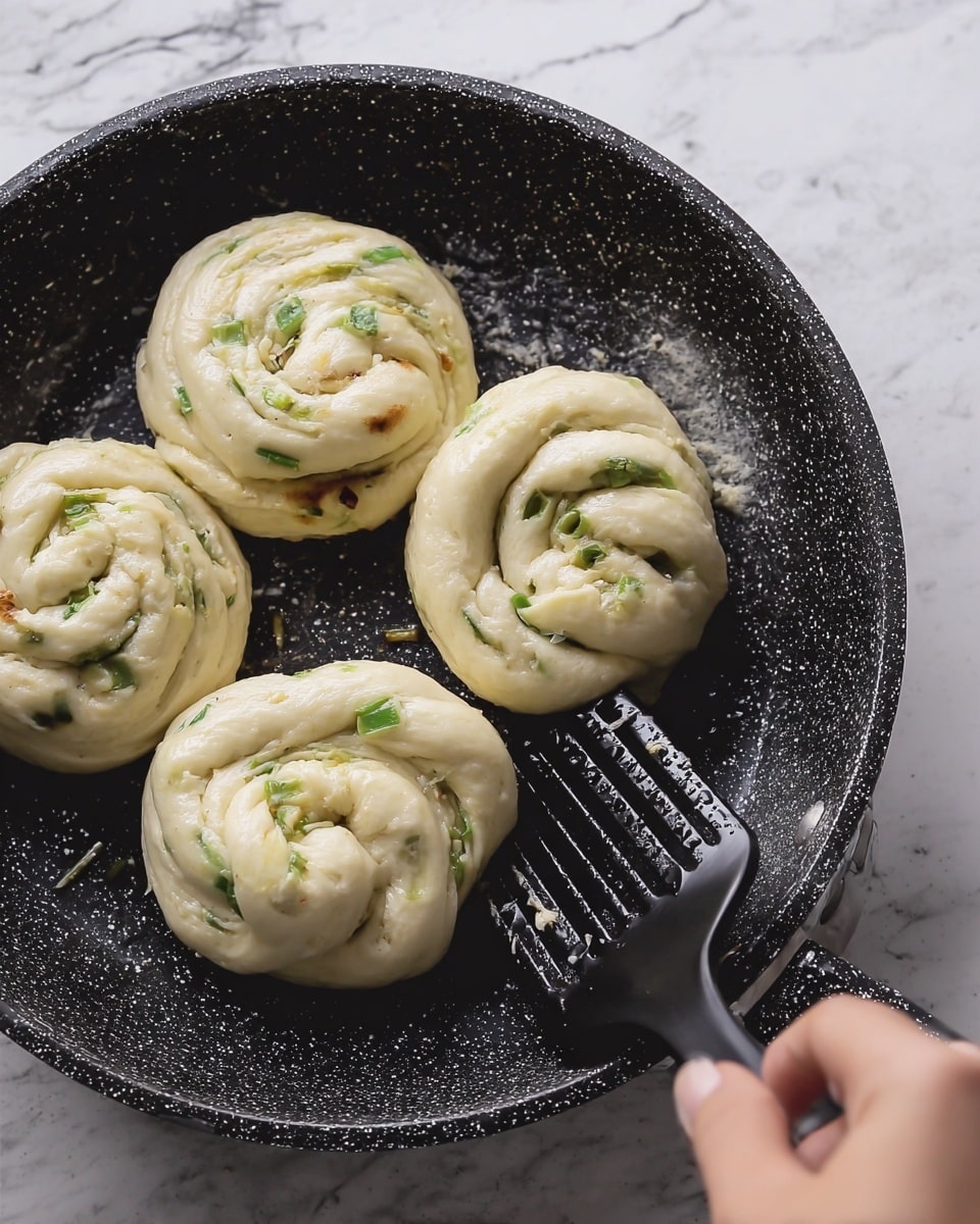 A white round plate holds seven small round buns arranged in a circle and one piece on top, all golden brown on top with sesame seeds and green onion bits. Inside each bun, the layers of soft dough can be seen, some with a twisted pattern. Next to the buns, a few pieces of golden fried dough are stacked on one side. There are three small black bowls on the plate, one with dark soy sauce, one with chopped green onions, and one with a brown powder. A woman's wooden spoon is dipping into the bowl with green onions. Around the plate, there are fresh ginger roots, lime wedges, and green leaves scattered on a white marbled surface with a grey cloth partially under the plate. Photo taken with an iphone --ar 4:5 --v 7