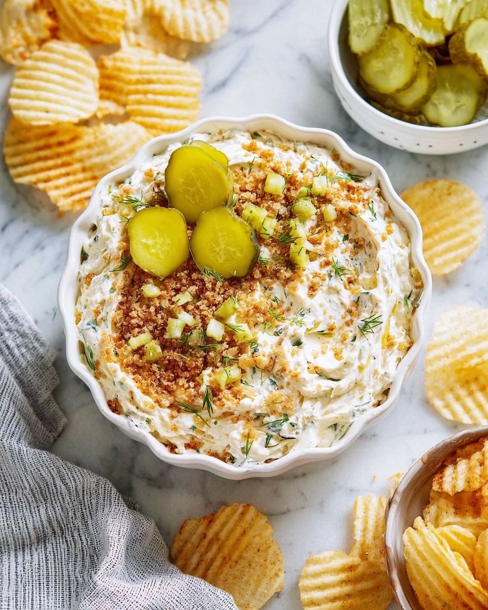 A close-up of a white bowl filled with a creamy white dip mixed with finely chopped green herbs, topped with golden-brown toasted crumbs sprinkled over the surface, and three round, green pickle slices arranged on one side. A woman's hand holds a ridged, light yellow potato chip dipped in the creamy mixture with some crumbs and green herb pieces visible on the dip. The bowl sits on a white marbled surface. photo taken with an iphone --ar 4:5 --v 7