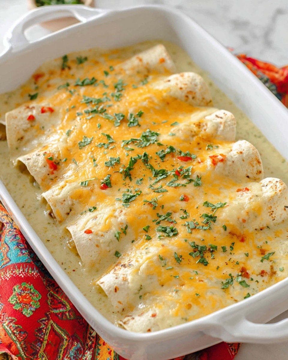 A white baking dish holds five rolled enchiladas side by side, covered in a creamy white sauce mixed with small green and red bits, likely chopped peppers. The top layer is melted golden cheese that is slightly browned in spots, sprinkled with small pieces of fresh green herbs for garnish. The sauce pools around the edges of the enchiladas, giving a smooth and rich texture contrast with the soft tortillas underneath. The dish rests on a white marbled surface with colorful cloth visible in the background. photo taken with an iphone --ar 4:5 --v 7