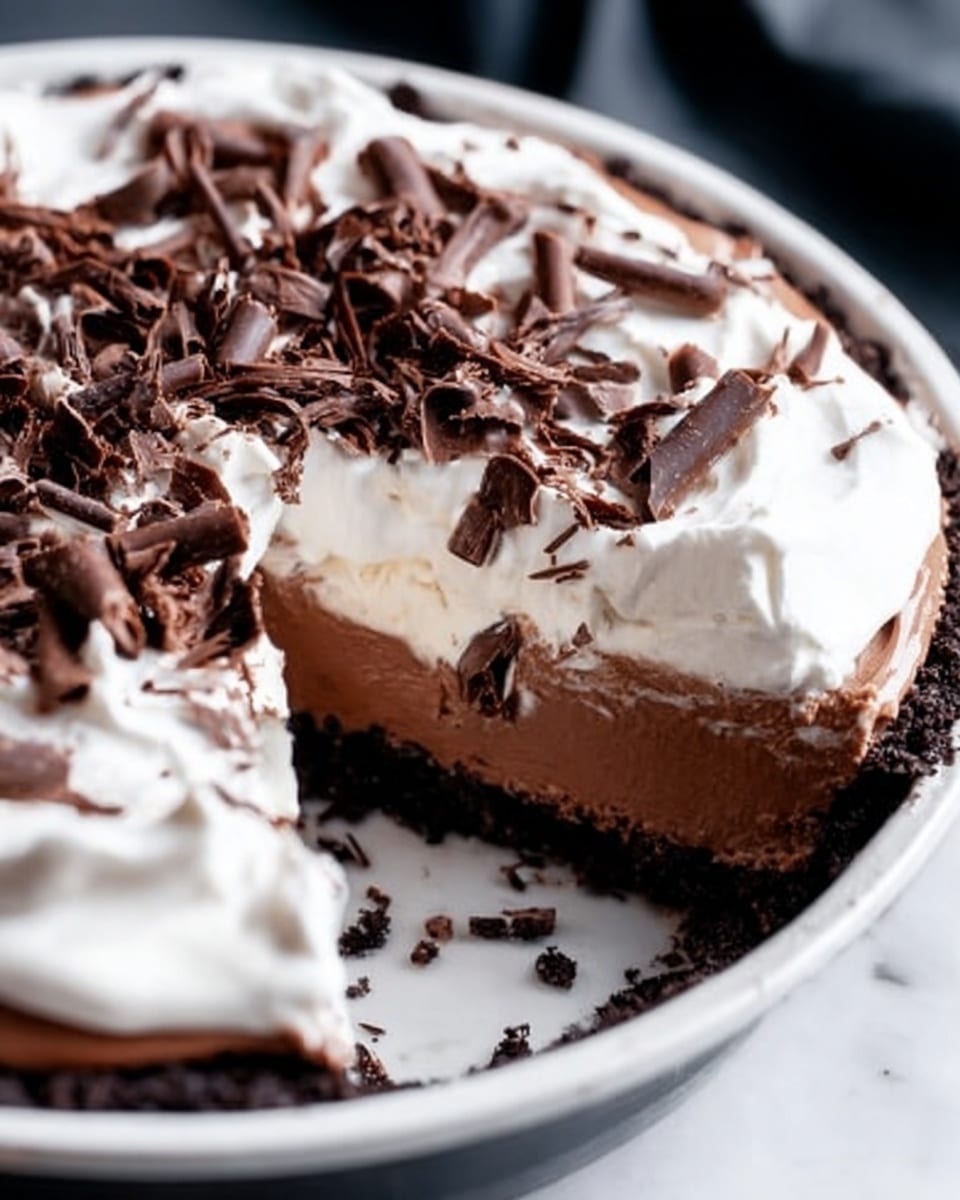 A slice of chocolate pie with three visible layers sits on a white plate placed on a white marbled surface. The bottom layer is a dark, crumbly chocolate crust, followed by a thick, smooth milk chocolate mousse layer in the middle. On top, there is a thin layer of white whipped cream, garnished with dark chocolate shavings scattered on and around the slice. In the background, a clear glass bottle filled with milk is softly blurred. The lighting is soft and natural, highlighting the textures of the pie. photo taken with an iphone --ar 4:5 --v 7