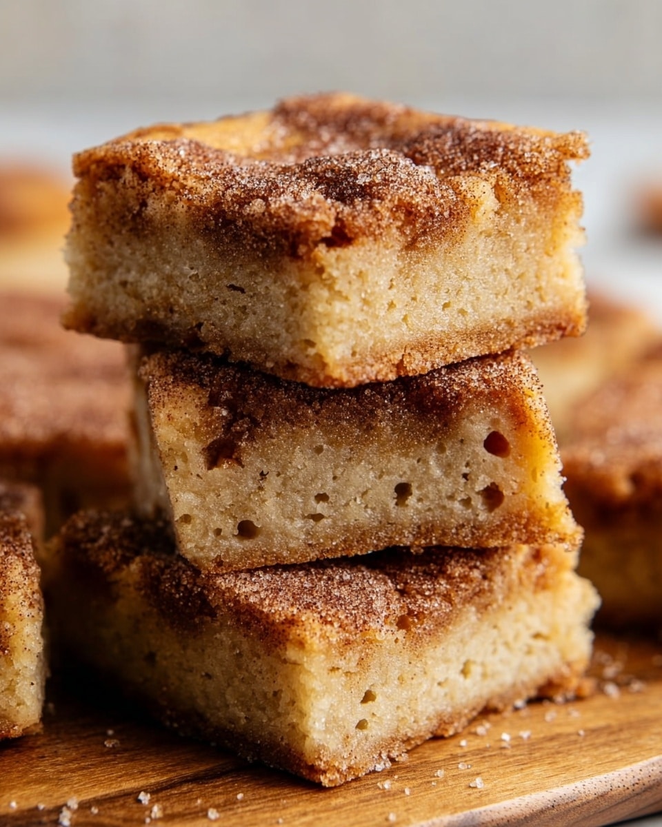 The image shows a close-up of a stack of three square pieces of cinnamon sugar blondies. Each piece has a moist, dense base layer that is light golden brown with small air holes visible. On top of each blondie is a thicker, rough-textured layer of cinnamon sugar with visible grains of sugar and specks of cinnamon, creating a darker brown crust. The stack is placed on a wooden surface with some more blurred blondie pieces in the background, all set on a white marbled texture. The edges of the blondies look slightly crisp and sugary, highlighting the contrast between the soft inside and crunchy top. Photo taken with an iphone --ar 4:5 --v 7