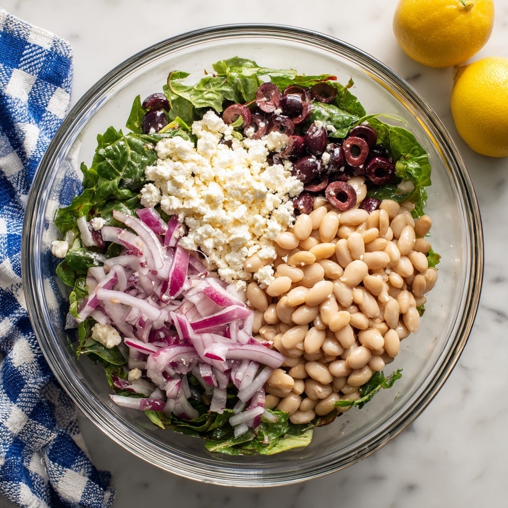 A fresh salad is served in a white bowl placed on a white marbled surface. The salad has many layers: the bottom layer is a mix of green diced cucumber and green bell peppers, followed by chunks of white cannellini beans spread evenly. Bright red halved cherry tomatoes are scattered on top, along with thin rings of light purple red onion. There are also black olive slices mixed throughout. White crumbled feta cheese is sprinkled over the salad, and the whole dish is lightly dusted with cracked black pepper and dried herbs. A gold spoon is resting inside the bowl, ready for serving. photo taken with an iphone --ar 4:5 --v 7